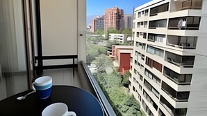 A balcony with two cups and a spoon, overlooking a cityscape with modern buildings and greenery. - Las Condes Apt | Prime Location + Fully Equipped (Las Condes)