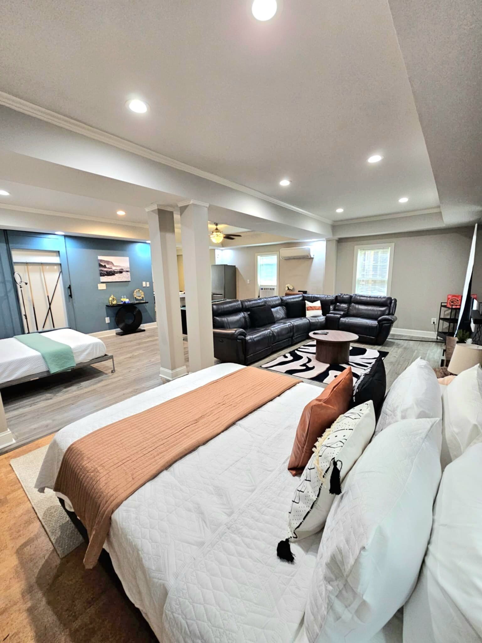 Ein geräumiger Raum mit einem großen Bett, einem Sofa und einem kleinen Couchtisch. Eine Tür führt in einen anderen Raum und ein Fenster mit Jalousien.