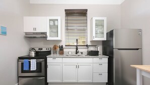 Una cocina moderna con armarios blancos, un refrigerador de acero inoxidable, un horno empotrado y una ventana con persianas.