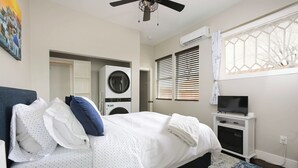 Un dormitorio con cama, lavadora, televisor y ventana con persianas.