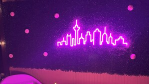 Una zona de estar acogedora con chimenea y un mural de horizonte urbano iluminado con neón.