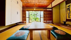 A traditional Japanese room with tatami flooring, a low wooden table, cushions with intricate designs, and sliding doors leading to a garden. - Fumiko-no-tei Residence with a view of the sea Max. 17 - 34 people OK. garden BBQ (西牟婁郡白浜町)