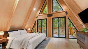 Quarto amplo com pé direito alto, uma cama grande, vigas de madeira e vista para o exterior.