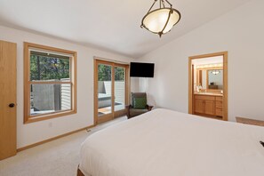 A bedroom with a large bed, a chair, a television, and a bathroom with a mirror and sink. - 15 Lassen - Charming, Hot Tub, SHARC, A/C (Sunriver)