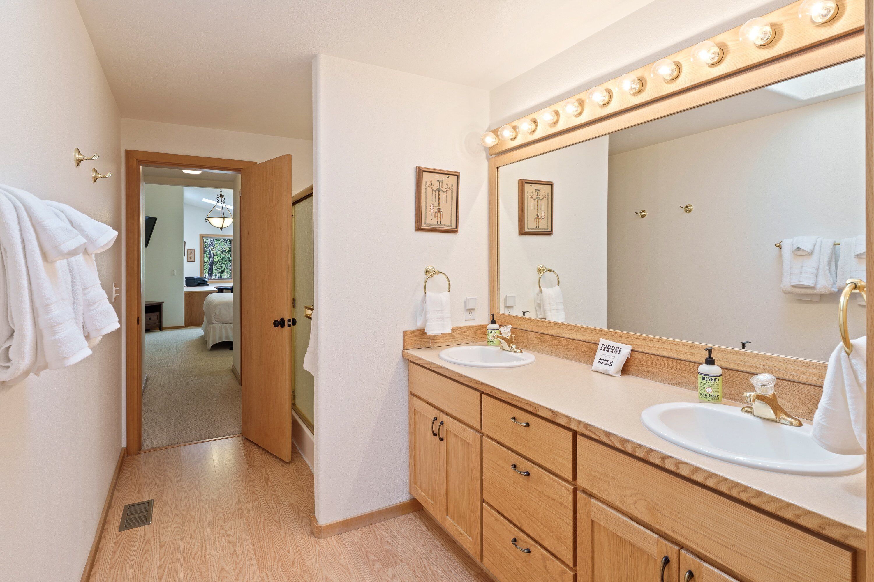 Une salle de bain avec des meubles en bois, un grand miroir avec éclairage intégré et un lavabo doté d’un robinet doré.