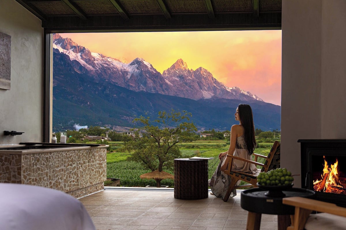 A room with a large window overlooking a mountainous landscape, a fireplace, and a seating area with a view.