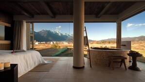 A bedroom with a large window, a bed, a stone bathtub, and a view of mountains. - Snow Mountain (Lijiang)
