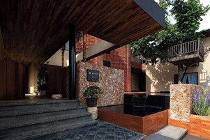 Un área exterior moderna con un muro de piedra, una pérgola de madera y una pequeña piscina.