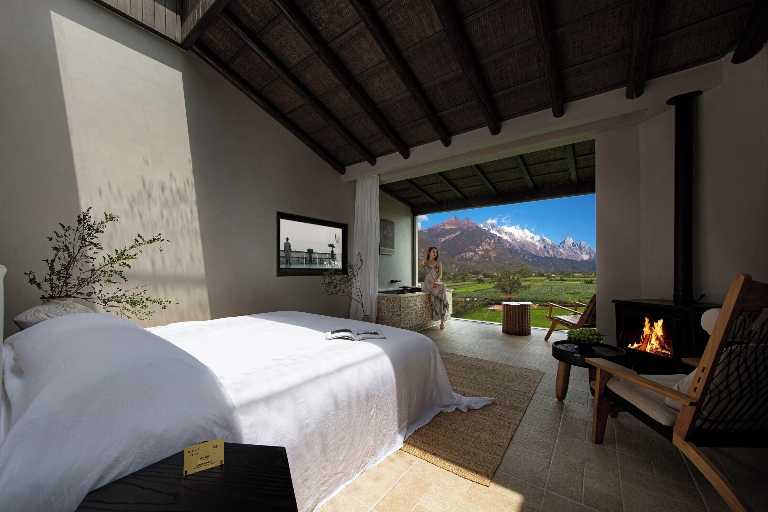 A bedroom with a bed, a wooden chair, a fireplace, and a view of mountains.