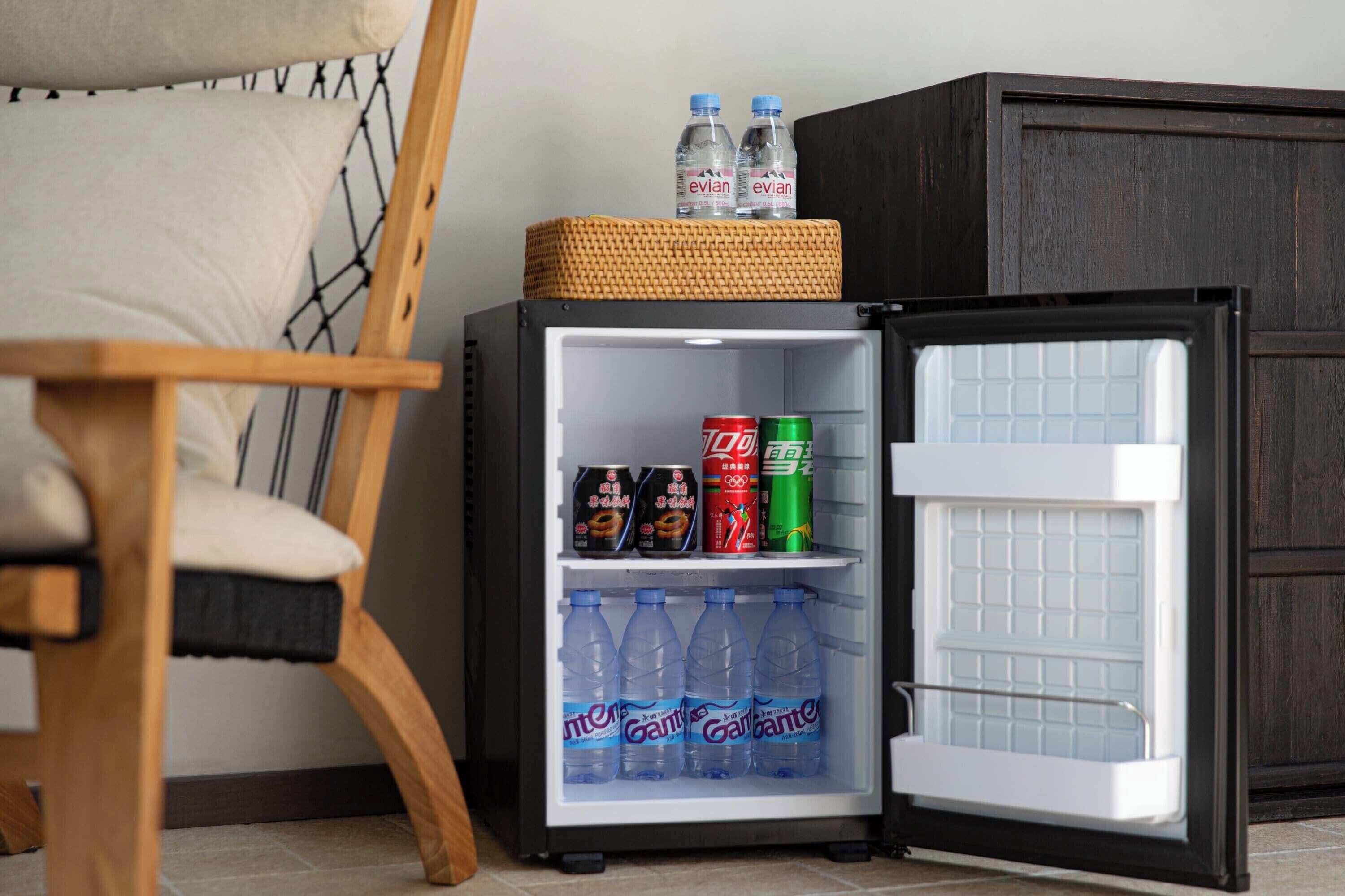A compact refrigerator with a basket on top, containing two bottles of water, a can of soda, and two cans of energy drink.