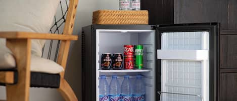 A compact refrigerator with a basket on top, containing two bottles of water, a can of soda, and two cans of energy drink.