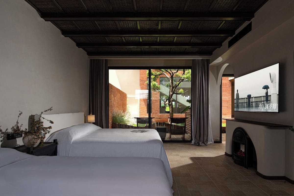 A hotel room with two beds, a TV, a fireplace, and a view of the outdoor area.
