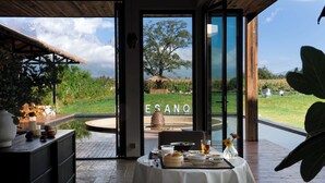 A dining area with a table set for two, a thatched roof structure, and a view of a grassy field with a mountain in the background. - Snow Mountain (Lijiang)