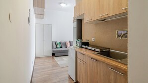 Eine kleine Küche mit Holzschränken, einem Einbauofen und einer Essecke mit einer grauen Couch.