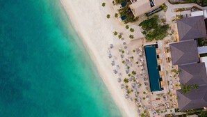 An aerial view of a resort with a large pool, sun loungers, and palm trees.