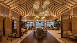 A spacious indoor area with a high wooden ceiling, multiple hanging chandeliers, and a view of the ocean.