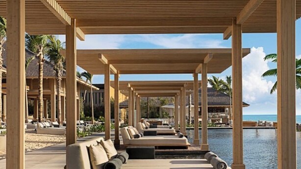 A covered outdoor seating area with a pool, wooden columns, and a view of the ocean.