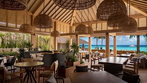An outdoor seating area with wicker pendant lights, wooden furniture, and large windows overlooking the ocean.