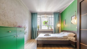 Ein Schlafzimmer mit einem Bett, einem grünen Kleiderschrank, einem Fenster mit Vorhängen und einer hängenden Pflanze.
