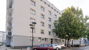 Ein mehrstöckiges Gebäude mit schlichter Fassade, mehreren Fenstern und einem Baum davor.