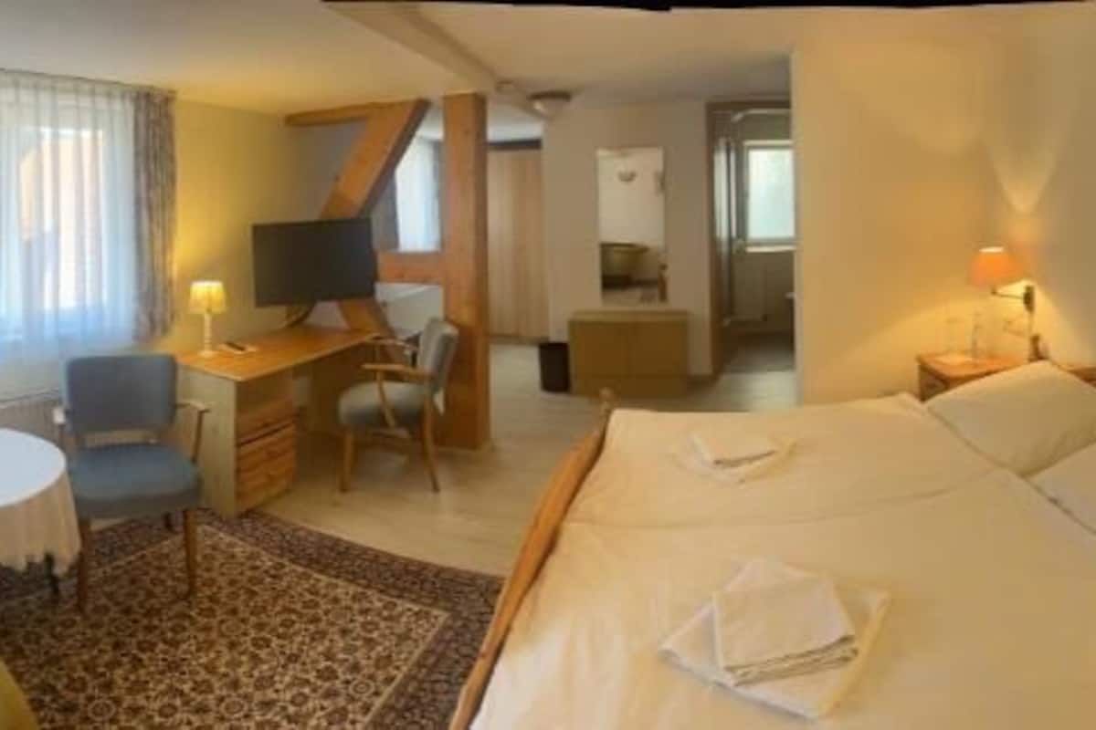 Een hotelkamer met een bed, nachtkastjes, een bureau met stoel, een klein rond tafeltje en een televisie.