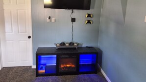 Una stanza con televisore a schermo piatto montato a parete, una console di gioco e un mobile TV a incasso con camino.