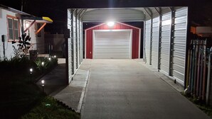 Ingresso di un garage coperto con una porta rossa, un vialetto in cemento e un'area ben illuminata da luci.