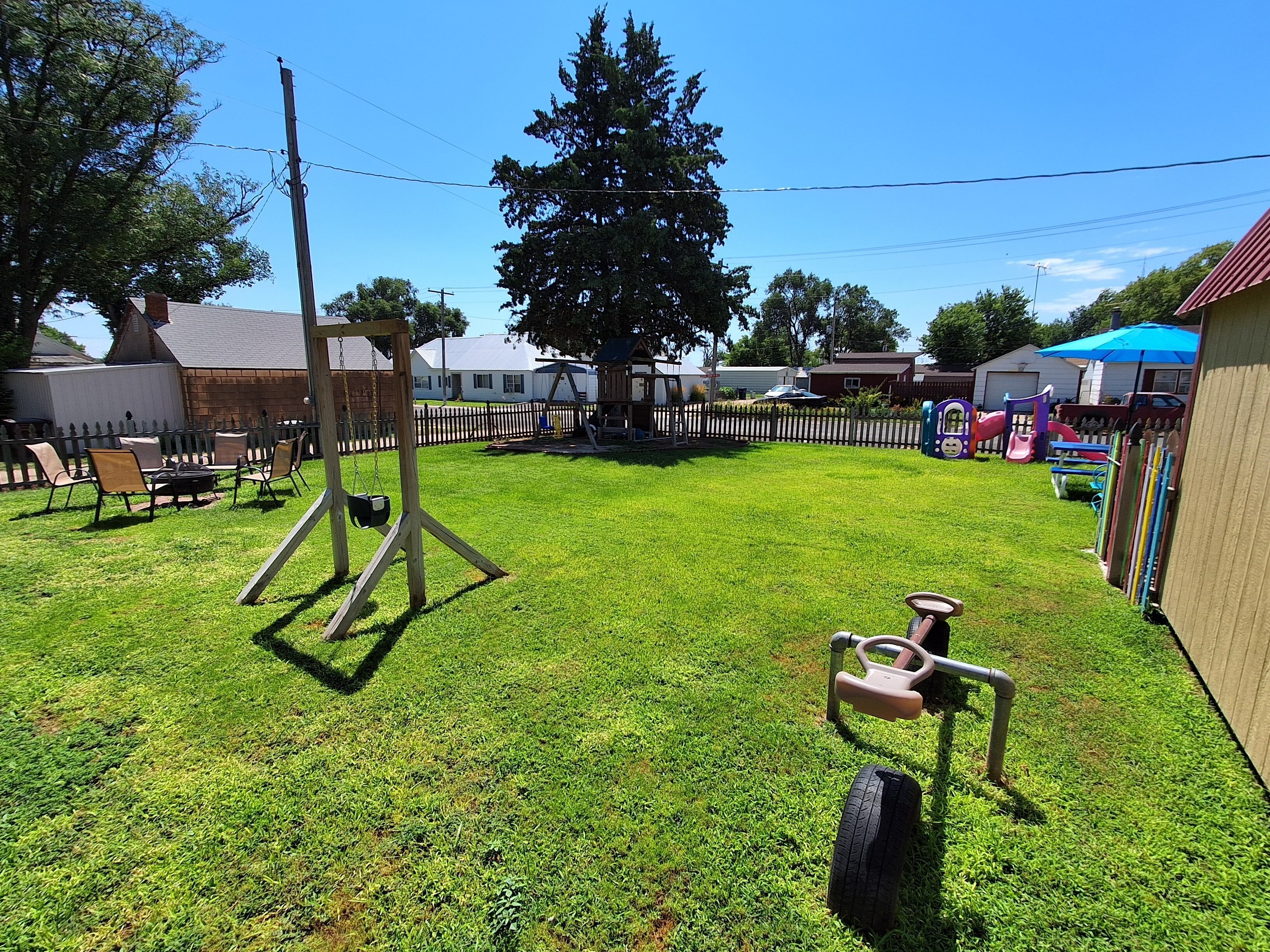 Un jardin arrière bien entretenu, avec une pelouse, une balançoire, un petit espace de jeux et une clôture.