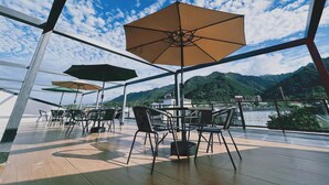 An outdoor terrace with tables and chairs, umbrellas, and a view of mountains.