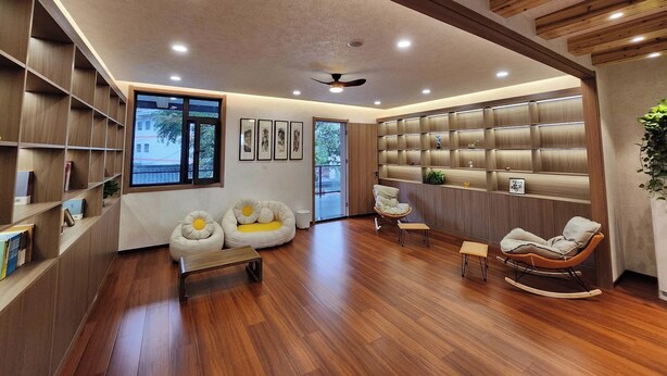 A modern living room with wooden flooring, built-in bookshelves, a seating area with a sofa and chairs, and a wall-mounted shelving unit.