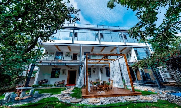 A modern two-story building with a glass facade, a covered outdoor seating area, and a landscaped garden with a water feature.