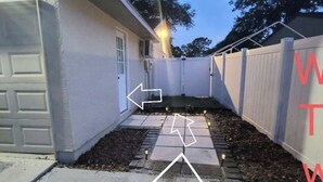 A residential backyard with a paved pathway, a wooden fence, and a garage door.