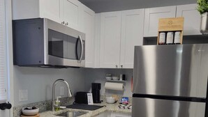 A modern kitchen with white cabinets, stainless steel appliances, a microwave, a coffee maker, and a refrigerator.