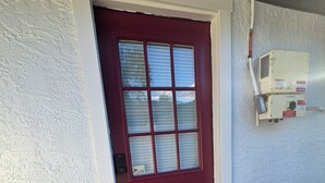 A red door with a window, a white textured wall, and a solar panel system mounted on the wall.