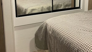 A bedroom with a large window, a bed with a checkered bedspread, and a wooden floor. - Convenient to UA, Northport and Mercedes (Tuscaloosa)