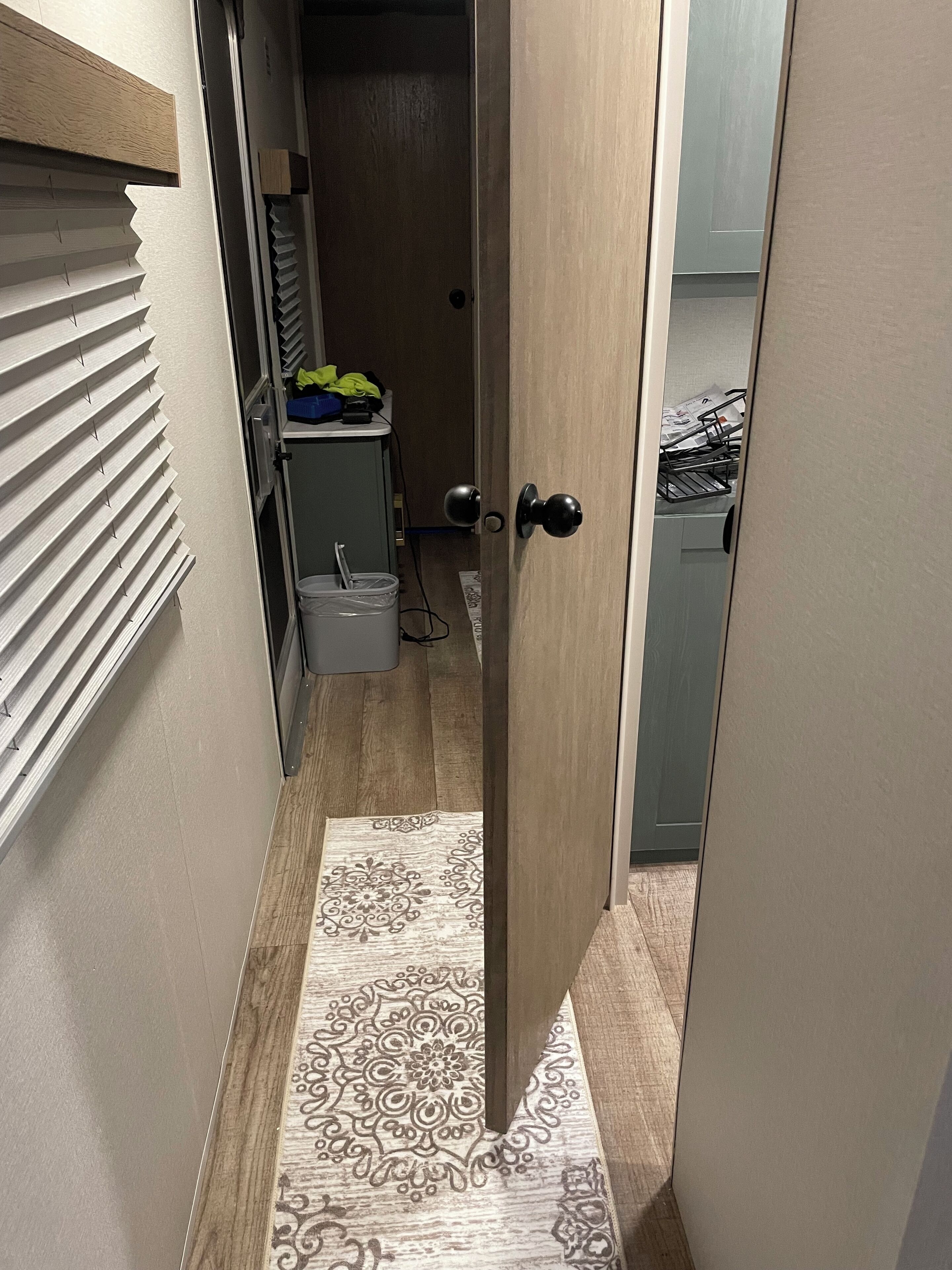 A narrow hallway with a wooden floor, a patterned rug, and a door leading to a room with a washing machine and a small cabinet.