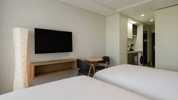 Habitación de hotel con dos camas, un televisor montado en la pared, una mesita con sillas y una lavadora en la esquina.