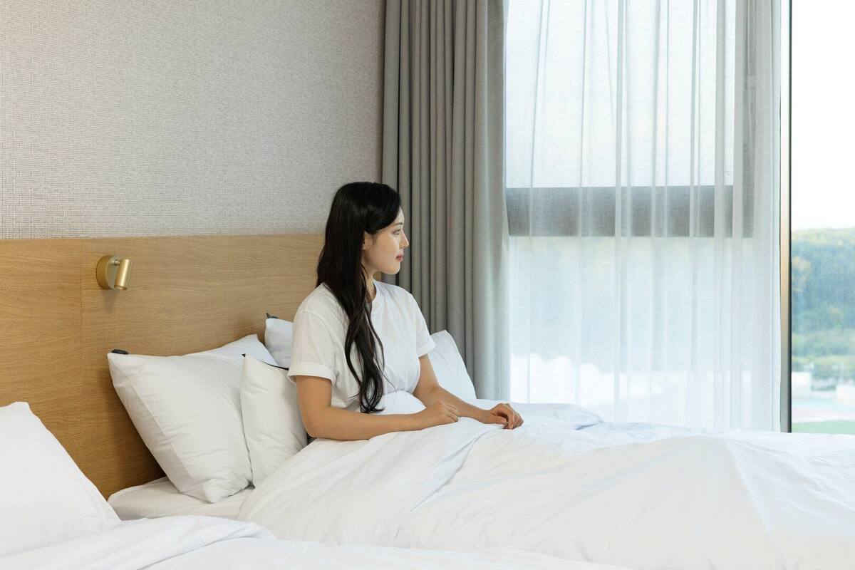 A hotel room with a large window, a bed with white linens, and a wooden headboard.