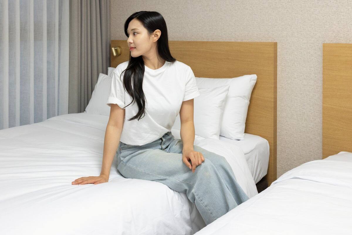 A hotel room with a bed, a wooden headboard, and a window with blinds.