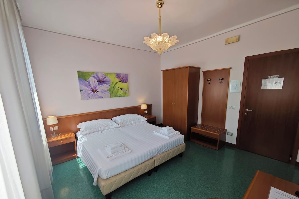 Una habitación de hotel con cama, escritorio, armario y un cuadro en la pared.