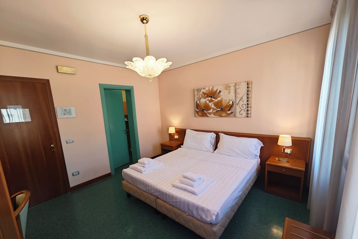 Habitación de hotel con una cama grande, dos mesitas de noche con lámparas, alfombra verde, puerta de madera y pared verde.