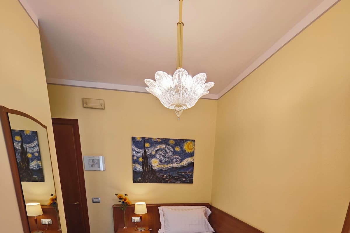 Una habitación de hotel con una cama, un escritorio, una silla, un cuadro y una araña.