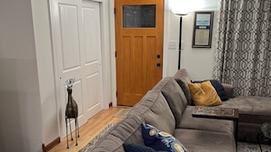 A living room with a grey sofa, a wooden door, and a framed picture on the wall. - Welcome FIFA! Nice 4-BR house, EZ Access to stadiums, PHL Airport, I95 & Transit (Claymont)