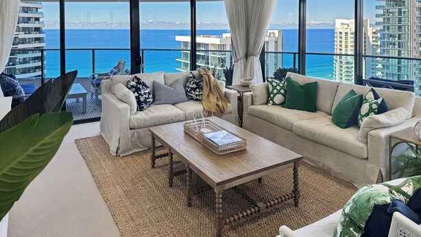 A modern living room with a large window overlooking the ocean and high-rise buildings. - Luxury Oracle Tower 2 Ocean Views 32nd floor (Broadbeach)
