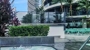 A swimming pool with a water fountain, surrounded by greenery and modern buildings. - Luxury Oracle Tower 2 Ocean Views 32nd floor (Broadbeach)