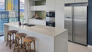 A modern kitchen with a large island, stainless steel appliances, and a view of a cityscape. - Luxury Oracle Tower 2 Ocean Views 32nd floor (Broadbeach)