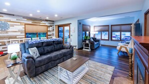 A modern living room with a grey sofa, a wooden coffee table, and a blue patterned rug. - Dockside Daze | Lakefront + Hot Tub | Sleeps 12, Stellar Sunsets (Bristol)
