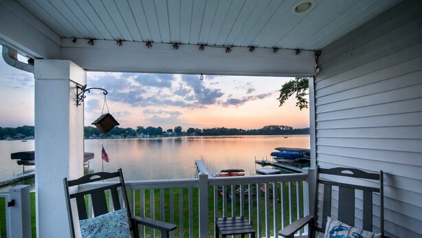 A covered porch with a view of a lake, outdoor furniture, and a flag. - Dockside Daze | Lakefront + Hot Tub | Sleeps 12, Stellar Sunsets (Bristol)