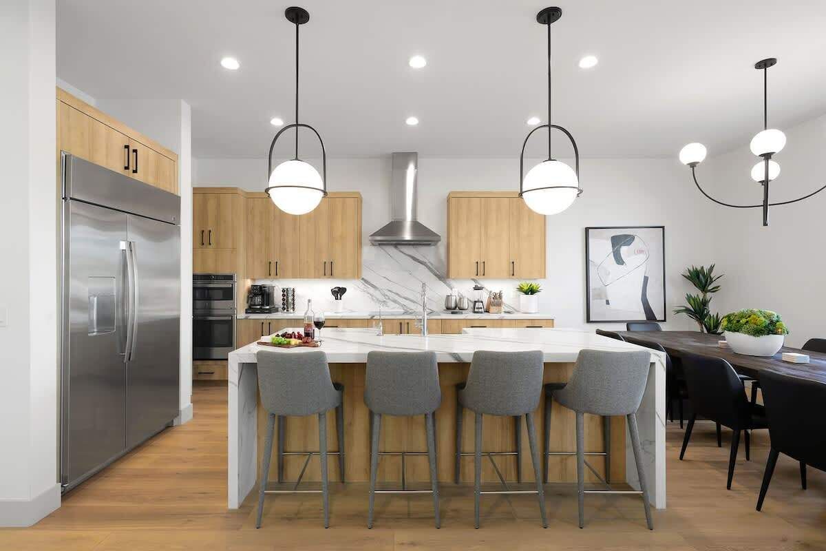 A modern kitchen with a central island, bar stools, stainless steel appliances, wooden cabinets, and pendant lighting.