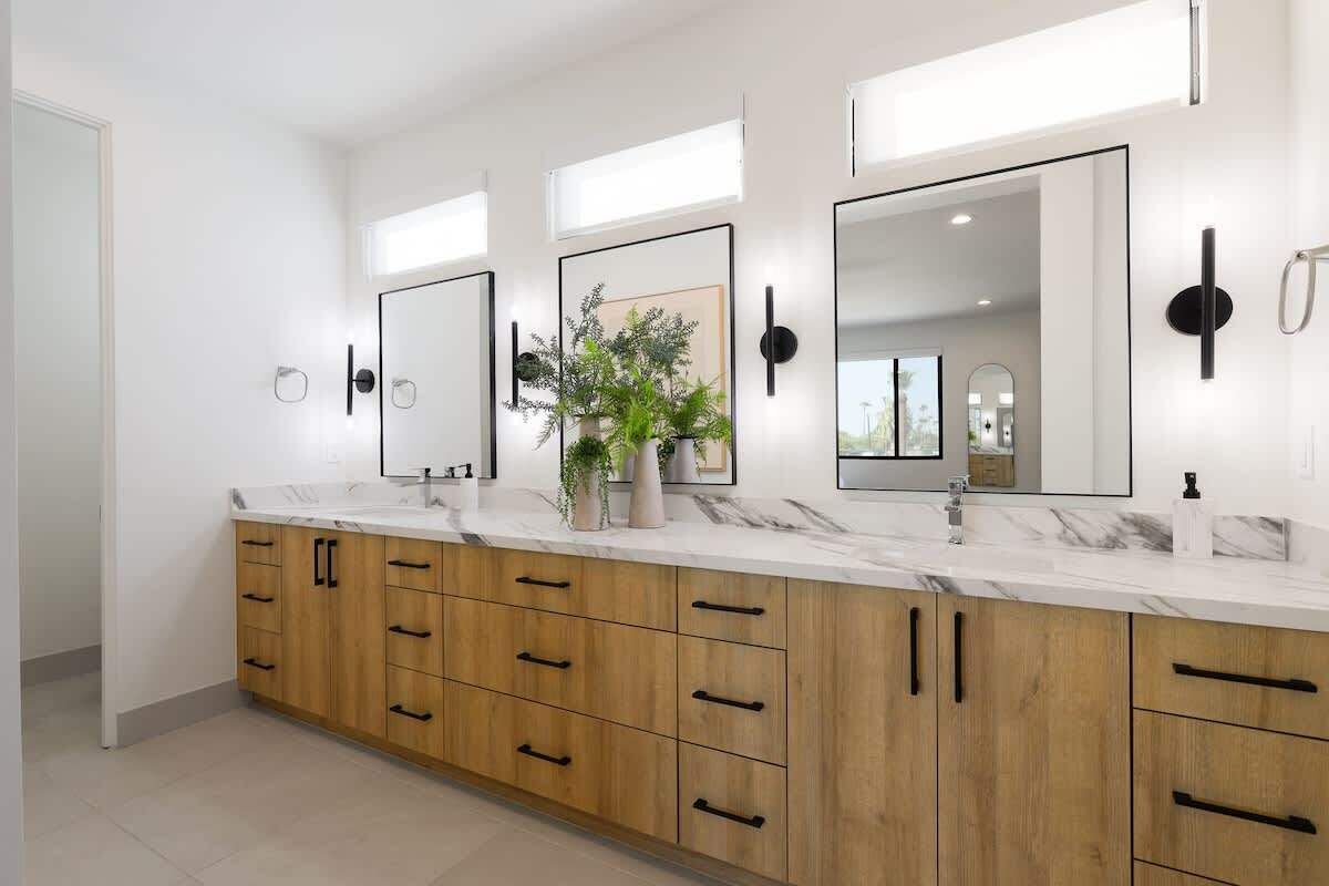 A modern bathroom with a marble countertop, wooden cabinets, and three large mirrors.